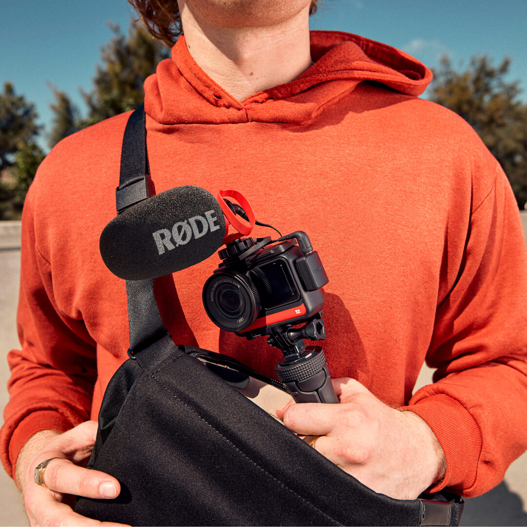 Skater wearing orange jumper and sling bag holding camera with VideoMicro II mounted on